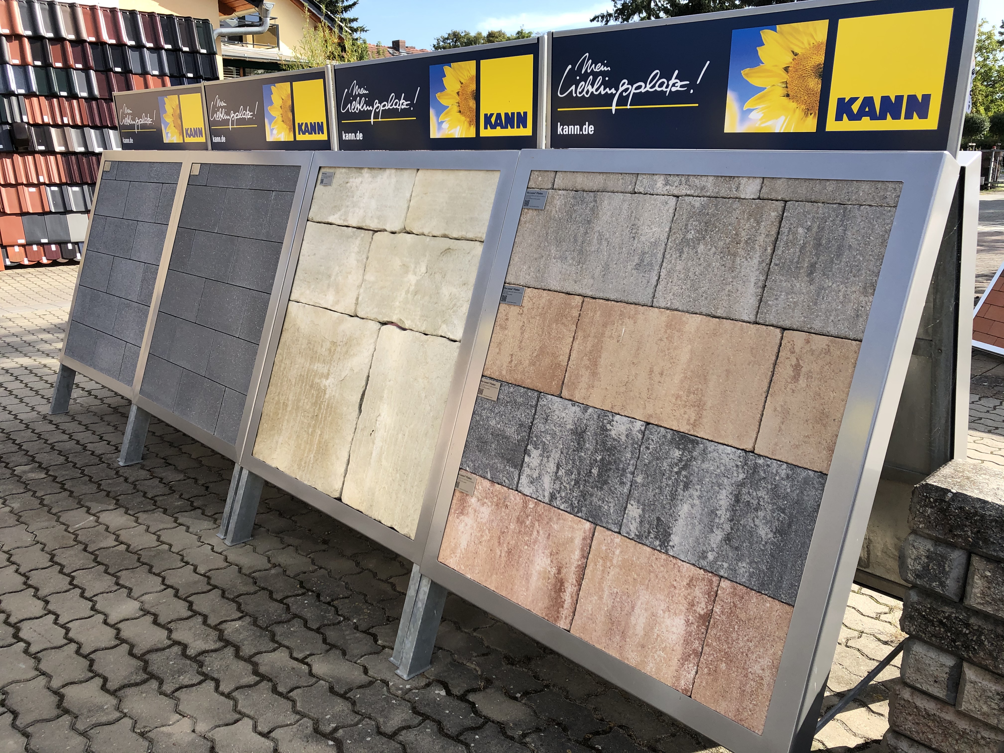Drei große Musterdisplays mit KANN Pflastersteinen in verschiedenen Farben auf einem Außengelände