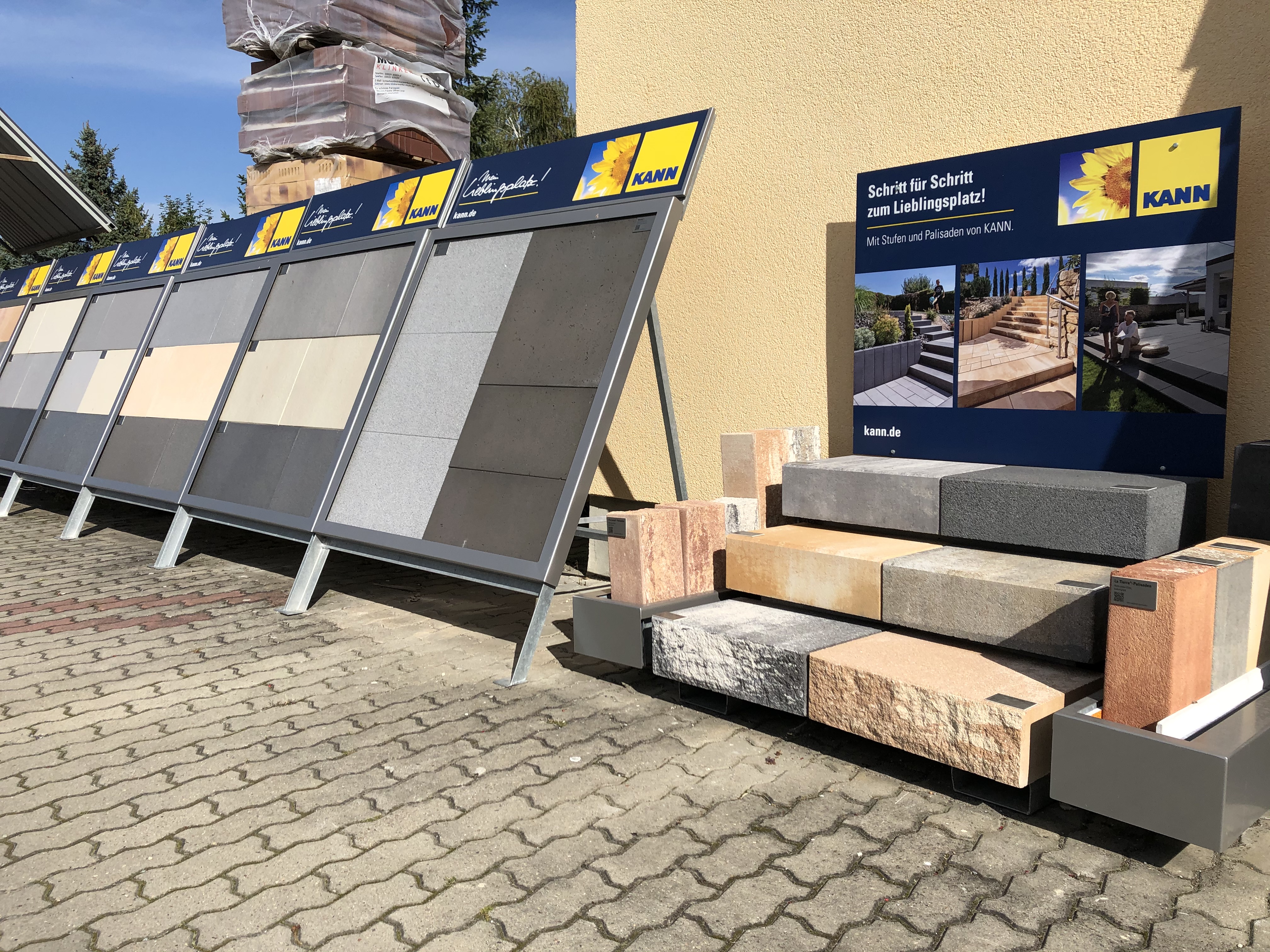 Verschiedene Modelle von Pflastersteinen und Palisaden der Marke KANN in einer Ausstellung im Freien