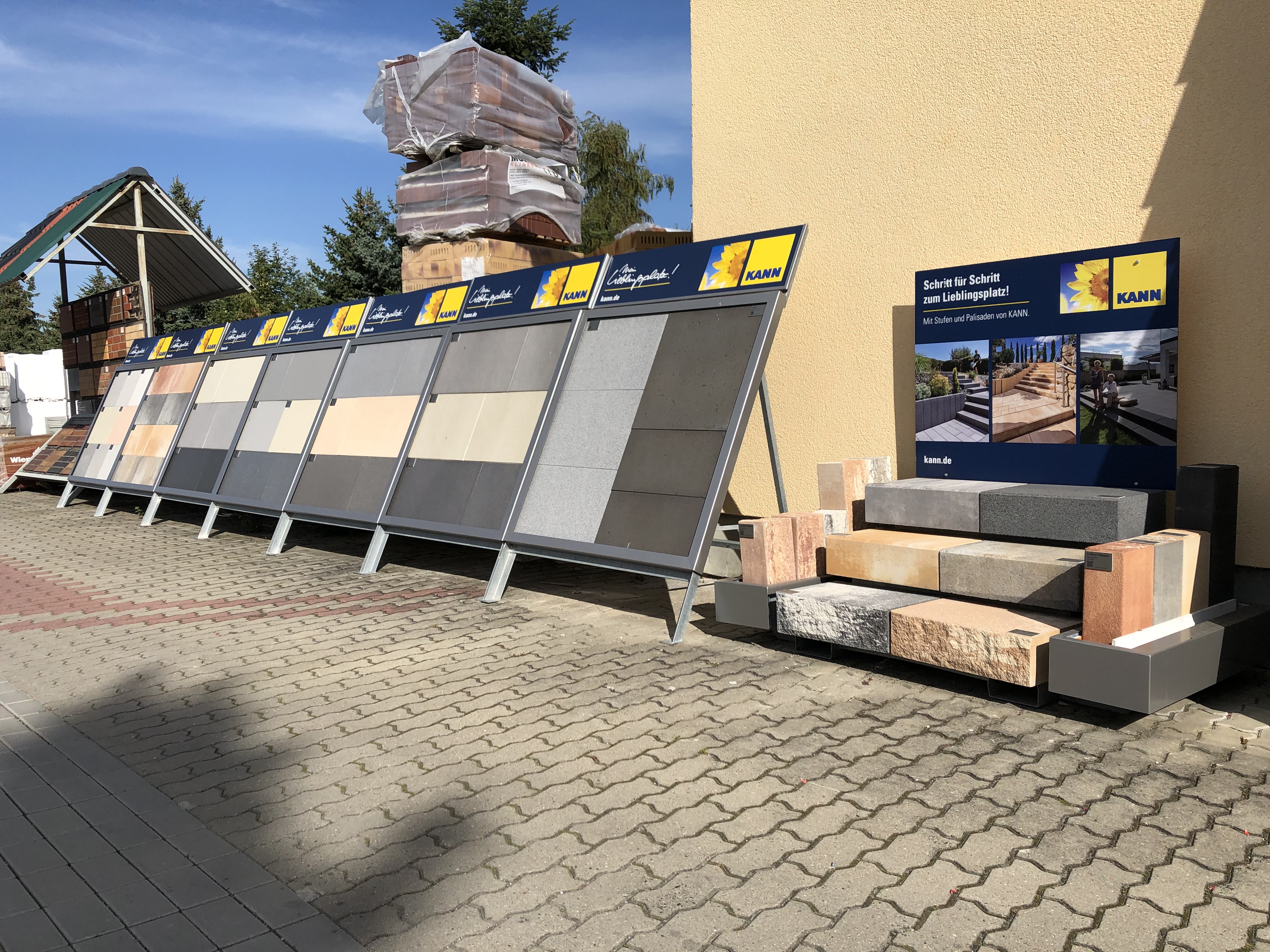 Außenbereich mit verschiedenen Mustern von Pflastersteinen und Mauersteinen auf Ausstellungstafeln und Stapeln in einem Baumarkt.