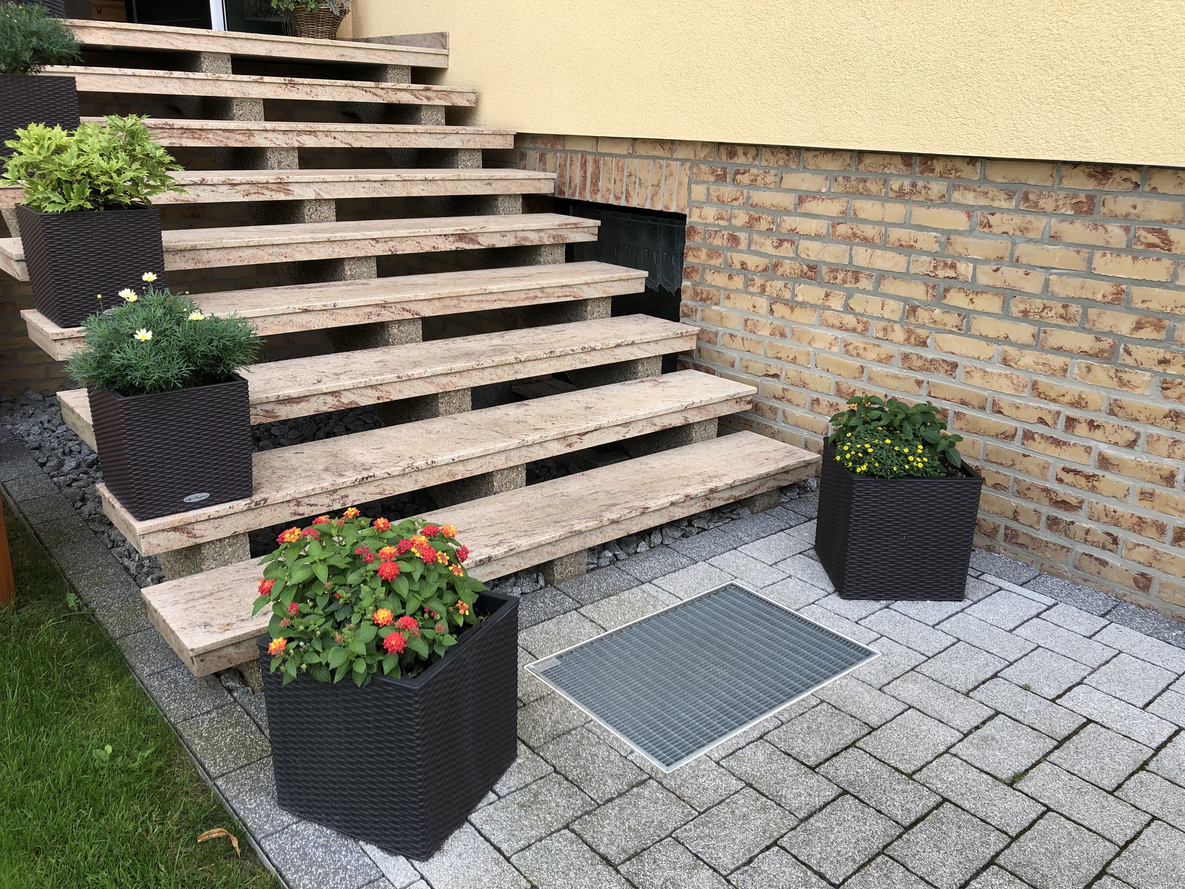 Steintreppe mit Pflanzen in modernen Rattankästen auf einer Terrasse mit Pflastersteinen und Ziegelwand