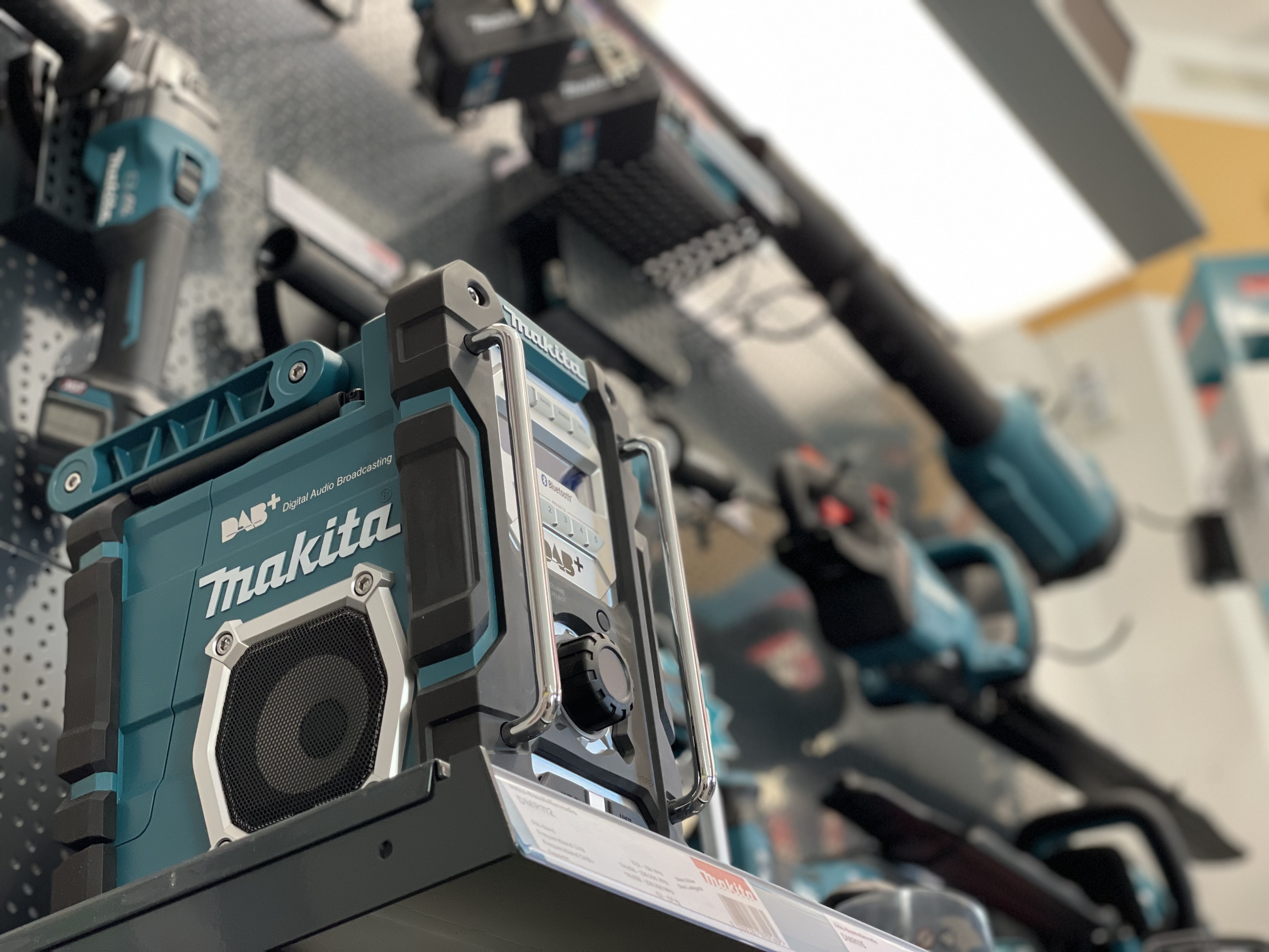 Ein Makita Baustellenradio DMR112 in einem Werkzeuggeschäft, umgeben von anderen Elektrowerkzeugen.